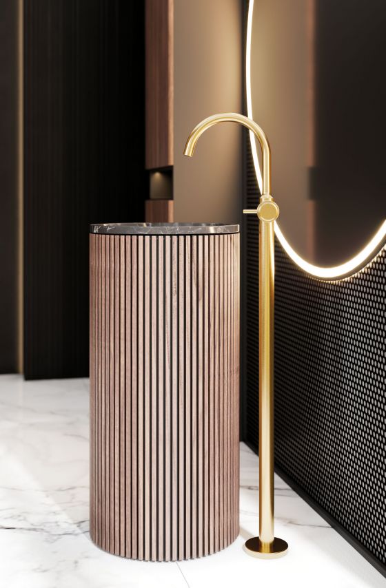Valencia, freestanding fitting in matt gold with metal handles, floor-standing washbasin clad with wooden elements in front of large, round, very decoratively lit mirror on a wall with accent mosaic in black-grey