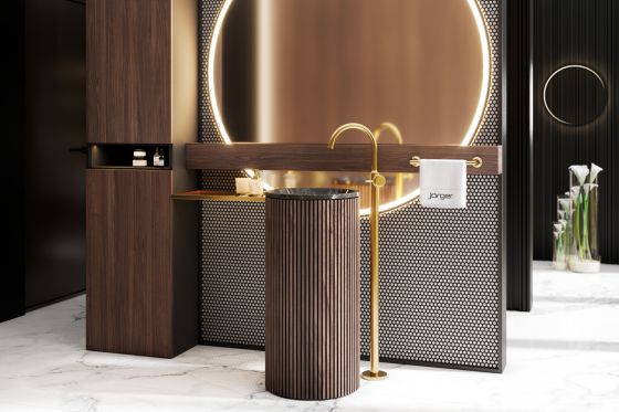 Valencia, freestanding fitting in matt gold with metal handles, floor-standing washbasin clad with wooden elements in front of large, round, very decoratively lit mirror on a wall with accent mosaic in black-grey